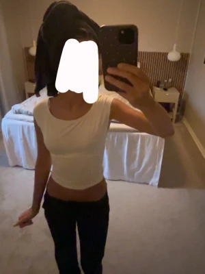 Vit croppad topp med knytband - Säljer en vit croppad topp med rund halsringning och knytband i midjan. Toppen är ärmlös och har en enkel, clean look som passar perfekt till jeans eller kjol. Materialet känns mjukt och stretchigt, troligen bomull eller polyester.