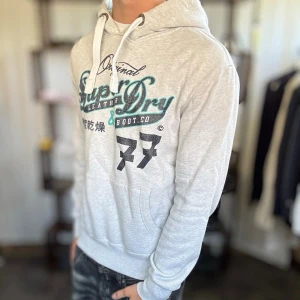 Superdry hoodie - Mycket fint skick, inga defekter. Nypris ca 1500kr. Passar dig som är 180-190cm ungefär. Modellen är 185 cm, 75 kg. Alltid billigare pris vid köp av flera varor‼️🙌Svarar alltid på frågor eller funderingar!  