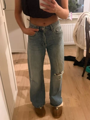 Zara Jeans  - Säljer ett par ljusblå raka jeans med medelhög midja och slitna detaljer på knä och bakficka. Jeansen är endast använda en gång. Storlek 32 men stora. Snygga slitningar både fram och bak. Från Zara 