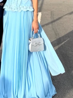 Ljusblå långklänning med spets corset - Elegant ljusblå långklänning med plisserad kjol och överdel i spets. Klänningen är axelbandslös och har en vacker, figurnära passform upptill. Perfekt för bal eller student. Matcha med silveraccessoarer för en extra glam look. Man kan justera den hur tight eller lös man vill ha den därav passar den flera storlekar 