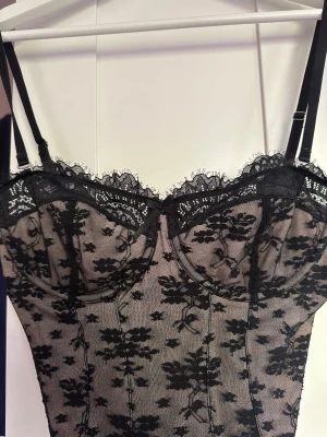 Svart spetsbody med blommönster från hunkemöller - Snygg svart body med transparent mesh och blommigt spetsmönster. Justerbara axelband och bygelkupor för extra stöd. Dekorativ spetskant upptill och figurnära passform. Inga tecken på användning förutom att tvättlappen är bortklippt. Den är från Hunkemöller i strl 75B eller Small. Går ej att köpa längre💕