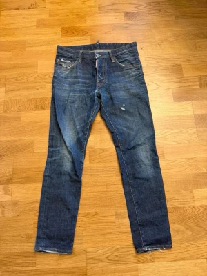 Blå jeans från Dsquared2 - Snygga blå jeans från Dsquared2 med slitningar och råa benslut. Klassisk femficksmodell med knappgylf och detaljerade sömmar. Jeansen har en smal passform och är tillverkade i denim med en cool tvätt. Slimfit 