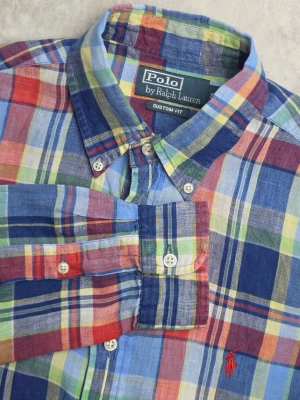Polo Ralph Lauren Custom Fit linneskjorta rutig flerfärgad storlek S - Rutig skjorta från Polo Ralph Lauren i Custom Fit-passform. Färgstarkt rutmönster i blått, rött, grönt och gult med button-down-krage och broderad röd Pony-logotyp på bröstet. Tillverkad i 100% linne för en lätt och luftig känsla.  Storlek S / S/P Custom Fit  Bra begagnat skick med viss noppning på en del ställen, se bilder för detaljer.  Mått Bröstbredd: ca 50 cm Plagglängd: ca 77 cm Axelbredd: ca 44 cm Ärmlängd: ca 65 cm  Material 100% linne
