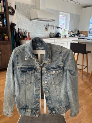 Blå jeansjacka  - Snygg acid wash jeansjacka från Gina Tricot med klassisk krage, knappar framtill och två bröstfickor med lock. Jackan har en cool, ljusblå tvätt och raka ärmar. Perfekt för dig som vill ha en tidlös och trendig look.