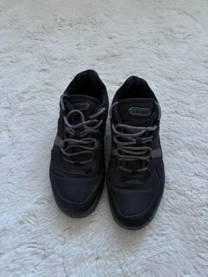 Svarta sneakers från Lacoste - Snygga svarta sneakers från Lacoste med grå detaljer och matchande grå skosnören. Skorna har en låg siluett och är tillverkade i en mix av textil och syntetmaterial. Pris kan diskuteras.