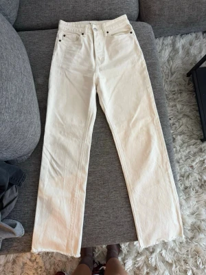 Raka vita jeans med rå kant - Snygga vita jeans med rak passform och hög midja. Jeansen har klassiska fem fickor och råa kanter nertill för en trendig look. Perfekta att styla med sneakers eller boots. Materialet är kraftig denim i bomull. Osäker på storlek men bör passa någon med storlek XS.