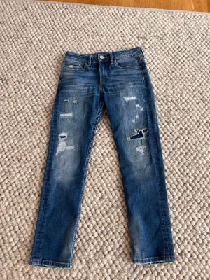 Blå slitna skinny jeans - Snygga blå skinny jeans med slitningar och hål på benen. Jeansen har klassisk femficksdesign, knapp och dragkedja framtill samt smal passform. Perfekta för en avslappnad och trendig look.
