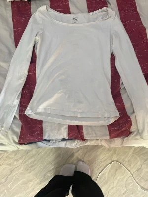 Vit långärmad topp med bred ringning - En enkel och stilren vit långärmad topp med bred ringning. Toppen har en smickrande passform och är perfekt att matcha med jeans eller kjol. Tillverkad i mjukt material som känns skönt mot huden.