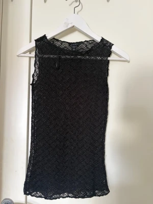 Svart spetsärmlös topp - Säljer en svart ärmlös topp i spets med transparenta detaljer. Toppen har en rund halsringning och ett elegant, figurnära snitt. Perfekt för dig som vill ha en stilren och trendig look.