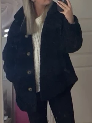 Svart teddyjacka - Mysig svart teddyjacka med stora knappar framtill och avslappnad, oversized passform. Jackan har bred krage och långa ärmar