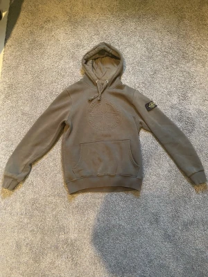 Stone Island hoodie - Snygg mörk grön hoodie från Stone Island med broderad logga på bröstet och klassisk patch på vänster ärm. Hoodien har känguruficka framtill och justerbar huva med dragsko. Perfekt för en avslappnad och trendig stil.