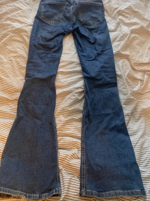 Blå bootcut jeans med utsvängda ben - Säljer ett par klassiska blå bootcut jeans med utsvängda ben och normal midja. Jeansen har två bakfickor och två framfickor, samt kontrastsömmar. Perfekta för dig som gillar retrostil och vill ha ett par jeans som sticker ut.