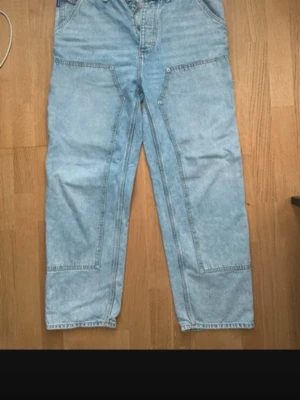 Ljusblå baggy jeans med stora fickor - Säljer ett par ljusblå baggy jeans med raka ben och stora, markerade fickor både fram och bak. Jeansen har en avslappnad passform och coola sömdetaljer, perfekta för en streetwear-look. Materialet är klassisk denim i bomull. 33/32
