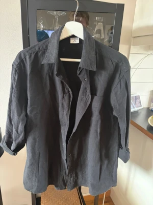 Svart linneskjorta från Stories XS - Snygg svart skjorta i linne från Stories i storlek XS. Skjortan har klassisk krage, knäppning framtill och en bröstficka. Perfekt för dig som gillar en enkel och stilren look.