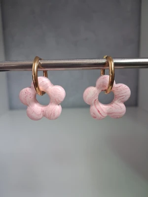 Rosa blommiga örhängen i jesmonite  - Säljer ett par söta örhängen med blommor i ljusrosa med marmorerade detaljer. Blomman är tillverkad i jesmonite och hänger på en rund ring i guldfärgad metall. Perfekta för dig som gillar lekfulla accessoarer och vill addera färg till din stil. Öronkroken är i rostfritt stål. Blomman är 2.5cm stor