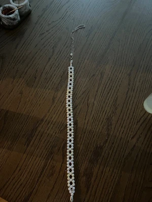 Pärlband med vita pärlor och kedja - Säljer ett långt pärlband med vita pärlor i två rader och silverfärgad kedja. Halsbandet har ett klassiskt och stilrent utseende, perfekt för att lyfta vilken outfit som helst. Låset är i metall och pärlorna är jämnt placerade längs hela bandet.