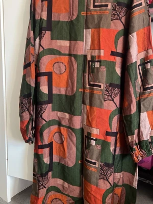 Långärmad tröja - Unik klänning/tröja med grafiskt mönster i grönt, orange, svart och beige. Långärmad modell med resår vid ärmslut. Tillverkad i ett mjukt bomullstyg som känns skönt mot huden. Perfekt för dig som gillar färg och retroinspirerad stil.