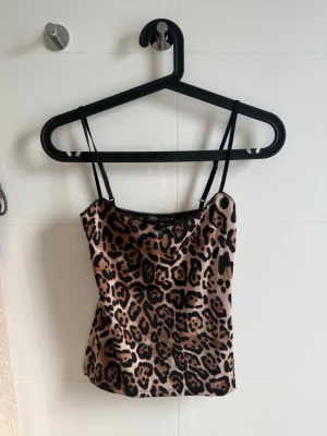 Leopardmönstrad linnetopp - Snygg linnetopp med leopardmönster och tunna svarta axelband. Toppen har en lätt glansig finish och en liten spetskant upptill för extra detalj. Banden är justerbara. 