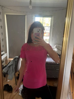 Rosa topp med spetsdetalj - Snygg rosa topp med korta ärmar och spets upptill vid halsen. Toppen har en rund halsringning. Perfekt för dig som vill ha en färgglad och söt look. (Obs har små fläckar som man kan se på en bild men de syns knappt)