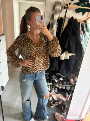 Leopardmönstrad blus med v-ringning - Säljer en luftig leopardmönstrad blus med v-ringning och långa, ballongformade ärmar. Blusen har en avslappnad passform och är tillverkad i ett tunt, transparent material som ger en cool och trendig look.