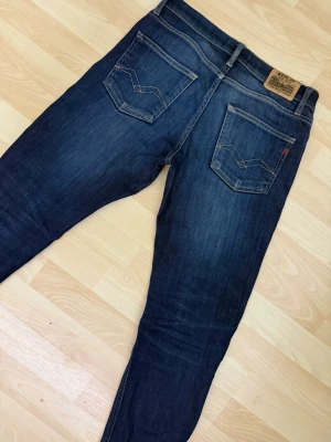 Mörkblå jeans från Replay - Snygga mörkblå jeans från Replay med klassisk femficksdesign och raka ben. Jeansen har kontrastsömmar och en läderpatch med logga bak i midjan. Tillverkade i slitstark denim som ger en tidlös look. 28/30