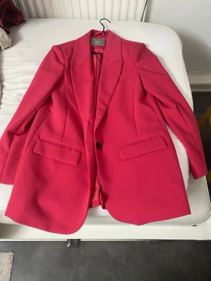 Rosa oversized kavaj Power Blazer - Snygg rosa oversized kavaj från The Power Blazer med klassisk krage och två framfickor med lock. Kavajen har en knapp framtill och är helfodrad. Perfekt för att lyfta vilken outfit som helst med en färgklick.