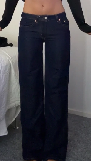 Mörkblåa vida jeans med hög midja - Säljer ett par mörkblåa jeans med hög midja och raka, vida ben. Klassisk femficksmodell med knapp och dragkedja framtill. Jeansen har en stilren look och är tillverkade i ett kraftigare denimtyg. Perfekta för dig som gillar en avslappnad men trendig stil.