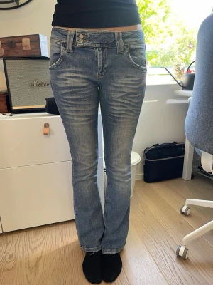 Blå bootcut jeans med slitningar - Säljer ett par blå bootcut jeans med snygga slitningar och tvättade detaljer. Jeansen har fyra fickor, dubbla knappar i midjan och klassisk dragkedja. Passar perfekt till en avslappnad och trendig stil. Det står att de är i storlek 28 i midjan men skulle säga att de är 1-2 storlekar större då de har töjts. OBS töjs inte mer. Modellen är 176 cm lång