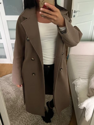 Brun lång kappa med skärp - Snygg brun kappa i en längre modell. Perfekta bruna färgen till hösten men kan nog funka på vintern då den är ganska varm. Har bara använts typ 3 gånger men väldigt varsamt.