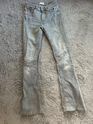 Grå bootcut jeans med slitningar - Säljer ett par grå bootcut jeans med lätt slitna detaljer och klassisk femficksmodell. Jeansen har normal midja och är tillverkade i denim med en mjuk känsla. Perfekta för dig som gillar en avslappnad men ändå trendig look.