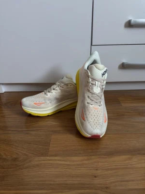 HOKA Clifton 9 Eggnog Passion – Storlek 45 1/3 - Riktigt läckra HOKA Clifton 9 i färgen Eggnog / Passion. Helt nya och aldrig använda. Perfekta för löpning, promenader eller vardagsbruk. Lätta och bekväma med bra stötdämpning.  • Märke: HOKA • Modell: Clifton 9 • Färg: Eggnog / Passion • Storlek: 45 1/3 • Skick: Helt nya, oanvända • Nypris: 1 999 kr  Skick enligt bilder. Hör gärna av dig vid frågor eller intresse.