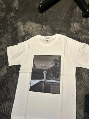 T-shirt med tryck - Säljer en stilren och snygg T-shirt med tryck från Fiore Studios   T-shirten är vit med ett snyggt vintageinspirerat tryck framtill. Enkel att matcha och passar perfekt till både jeans och shorts.  Bilderna / trycket är gjort med presstekniken sublimering. Vilket betyder att trycket färgas i själva fibrerna / trådarna på tyget och INTE som ett plastigt lager ovanpå tyget.   Storlek: S - aldrig använd