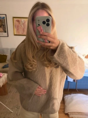 Mohair - Mysig beige stickad tröja med oversized passform och långa ärmar. Tröjan har en enkel design med rund halsringning och är perfekt för lager på lager. Materialet ser fluffigt och mjukt ut, vilket gör den extra skön att bära under kyliga dagar.