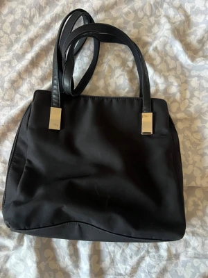 Svart axelväska med silverdetaljer - Superfin och extremt praktisk vintage "organizer"-handväska från det amerikanska märket Worthington. Tillverkad i ett slitstarkt, svart nylon/mikrofiber-material med snygga silverfärgade detaljer – en perfekt representation av det sena 90-talets och tidiga 00-talets (Y2K) minimalistiska stil. Den har ett dragkedjesystem som gör att den kan öppnas upp helt och avslöjar en fantastisk organisatör: massor av fack, inbyggda kortplatser, ID-fönster osv. 27x24 cm