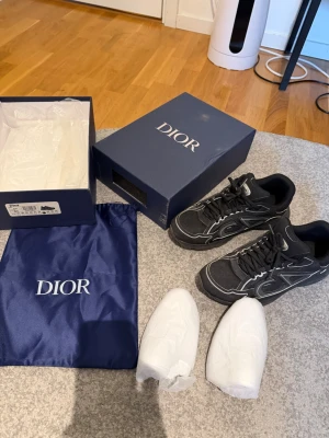 Svarta sneakers med vita detaljer - Säljer ett par svarta sneakers med vita kontrastdetaljer och meshpaneler. Skorna har en chunky sula och tydlig logga på sidan. Medföljer originalkartong och dustbag. Perfekta för dig som vill ha en exklusiv och trendig look. Skorna rengörs såklart innan frakt! 