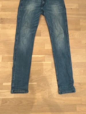 Blå slim fit jeans med slitningar - Ett par blå slim fit jeans med snygga slitningar och tvättade detaljer. Jeansen har klassisk femficksdesign och raka ben. Perfekta för en avslappnad och trendig look. Modell Ambass slimfit. Funkar för både 31 och 32 i midjan. 
