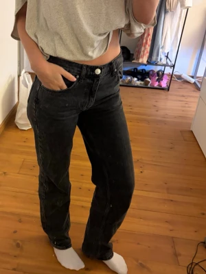 Svarta raka jeans med hög midja - Säljer ett par svarta jeans med rak passform och hög midja. Jeansen har klassisk femficksdesign, bälteshällor och knappgylf. Materialet är kraftigt denim som ger en snygg vintagekänsla. Perfekta till en avslappnad och trendig look.