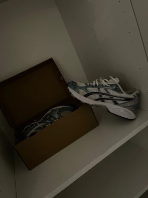 Vita och grå sneakers med meshdetaljer - Snygga sneakers i vitt och grått med meshpaneler och svarta detaljer. Skorna har en sportig siluett, tjock sula och klassisk snörning. Perfekta för dig som gillar en trendig och bekväm stil.