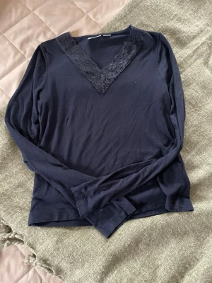Mörkblå långärmad topp med spets - Snygg mörkblå långärmad topp från Gina Tricot med v-ringning dekorerad med spetsdetaljer. Perfekt för dig som gillar en enkel men ändå elegant stil. Tillverkad i mjukt material som känns skönt mot huden.