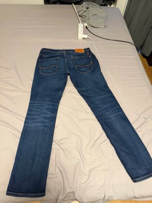 Jack and jones jeans med sjuk fading  - Storlek 30/32, regular/clark modell. Snygga mörkblå jeans med raka ben och klassiska kontrastsömmar. Jeansen har fem fickor och en läderpatch bak i midjan. Tillverkade i slitstarkt denimtyg som ger en tidlös look.