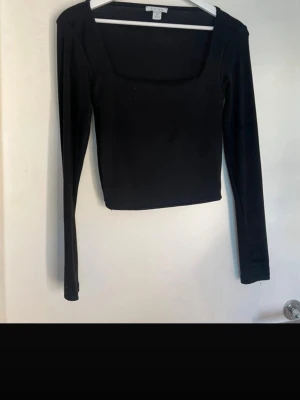 Svart långärmad topp från Amisu - Snygg svart långärmad topp från Amisu med fyrkantig ringning. Toppen har en tight passform och är tillverkad i mjukt, stretchigt material som sitter skönt på kroppen. Perfekt att styla med jeans eller kjol för en clean look. Storleken är M men sitter mer som xs/s