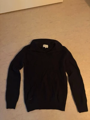 Mörkblå stickad tröja från Norvie - Mysig mörkblå stickad tröja från Norvie med lång ärm och hög krage. Perfekt för kyliga dagar och enkel att matcha med jeans eller kjol. Tröjan har en klassisk passform och ribbade muddar vid ärmslut och nederkant. Inte använd mycket 