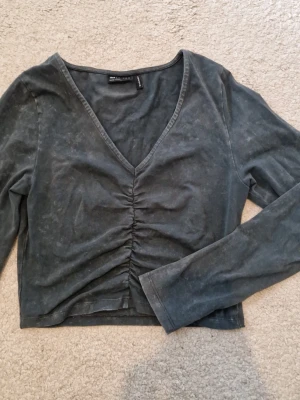 Mörkgrå croppad topp - Mörkgrå croppad topp med v-ringning och snygg rynkning framtill. Långärmad modell i mjukt material. Enkel men ändå unik detalj framtill. Tvättad look.