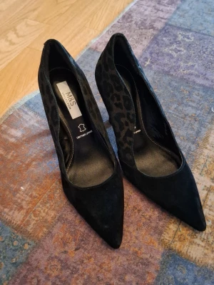 Svarta pumps med leopardmönster - Snygga svarta pumps från M&S Collection med spetsig tå och leopardmönstrade sidor. Ovandelen är i mockaliknande lädermaterial och insidan är märkt med 'leather upper'. Perfekta för dig som vill ha en cool och trendig look.
