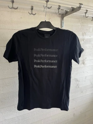 Svart Peak Performance t-shirt - Snygg svart t-shirt från Peak Performance med tryck framtill i flera rader. Klassisk rund hals och korta ärmar. Perfekt till jeans eller shorts för en clean och enkel stil.