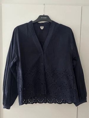 Broderad blus från Arket - Snygg mörkblå blus med v-ringning och knappar framtill. Blusen har långa ärmar och fina broderade håldetaljer längs nederkanten som ger en unik look. Dessvärre har blusen efter ex antal tvättar blivit missfärgad på högerarmen (se bild)💙💟