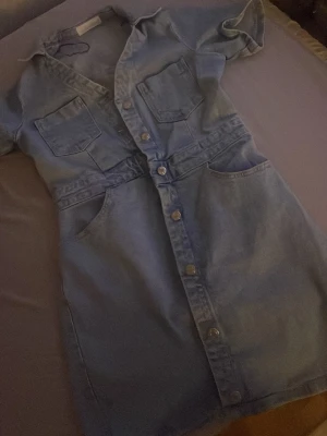 Ljusblå jeansklänning från ZARA - Säljer en ljusblå jeansklänning från ZARA med kort ärm, knappar framtill och stora fickor både på bröstet och vid höfterna. Använd två gånger 