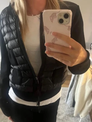 Svart cardiganjacka från Moncler - Snygg svart cardiganjacka från Moncler med quiltad framsida och mjuka stickade ärmar. Jackan har dragkedja framtill, rund halsringning och två fickor på magen. Perfekt för lager på lager och en stilren look.