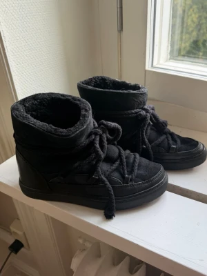 Inuikii vinterskor  - Säljer ett par svarta kängor med högt skaft och grova snören. Insidan är fodrad med mjukt, fluffigt material som håller värmen. Yttermaterialet är en mix av mocka och läderimitation. Perfekta för kalla dagar och riktigt snygga till jeans eller tights.
