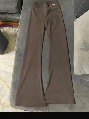 Bruna utsvängda leggings - Snygga bruna leggings med utsvängda ben och hög midja. Perfekta för dig som gillar en bekväm och trendig stil. Materialet är stretchigt och mjukt, vilket gör dem sköna att bära hela dagen. Liten logga framtill vid midjan.
